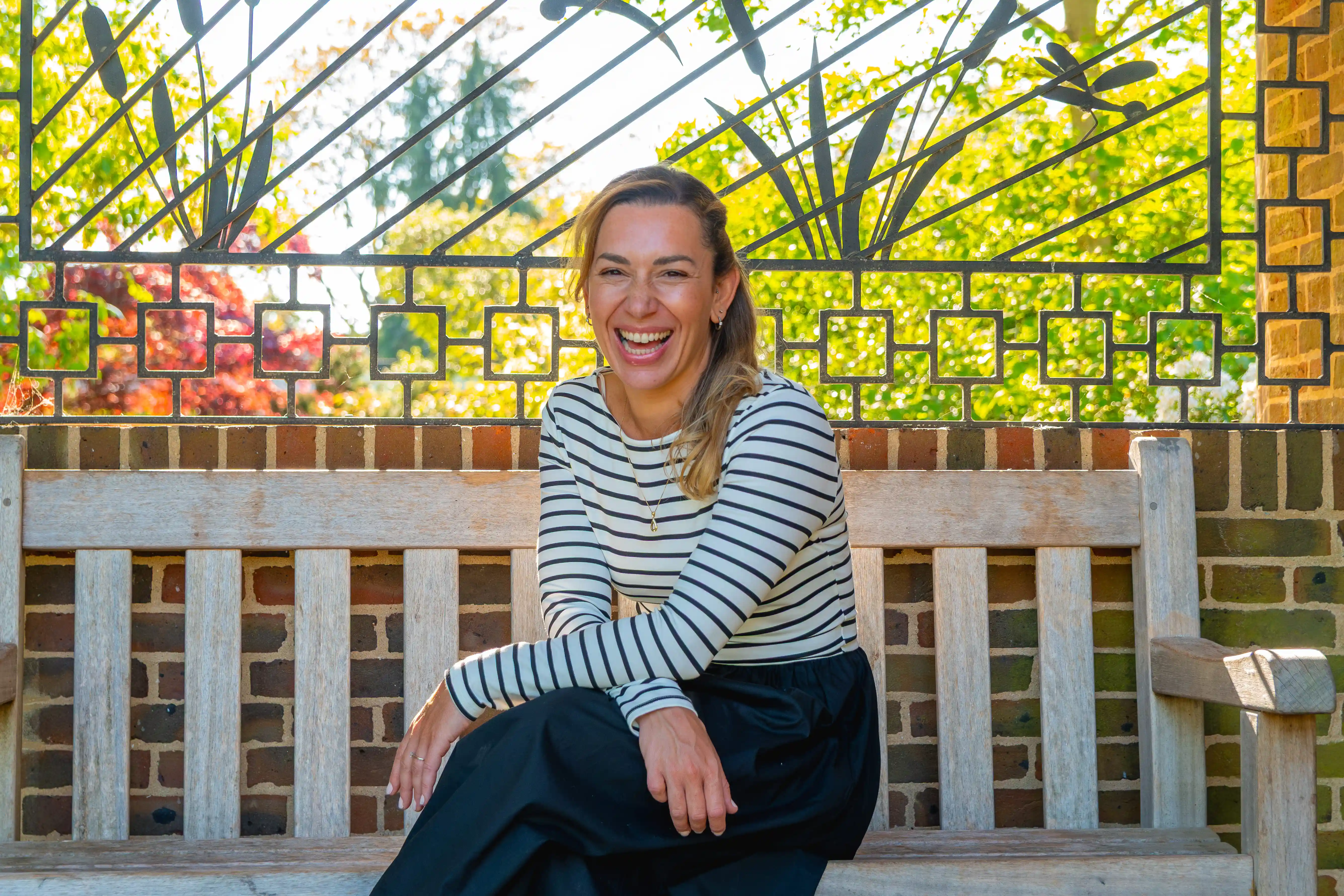 A female coach sits on a bench in a colourful garden laughing